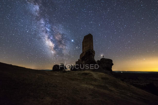 De baixo irreconhecível turista explorando arruinado castelo medieval sob céu estrelado com Via Láctea à noite — Fotografia de Stock