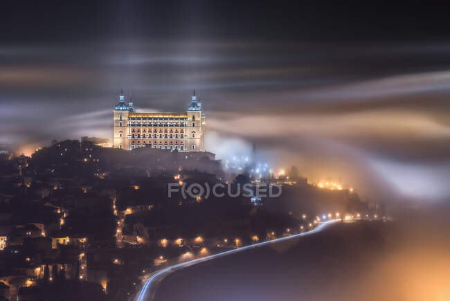 From above amazing scenery of illuminated ancient Alcazar de Toledo castle over town in misty twilight — Stock Photo