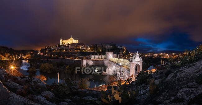 Splendido scenario di palazzo antico illuminato costruito sopra la città nella notte colorata a Toledo — Foto stock