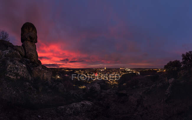 Вид зверху на анонімного мандрівника, що стоїть на скелі і дивиться на світле стародавнє місто під барвистим хмарним небом на світанку — стокове фото
