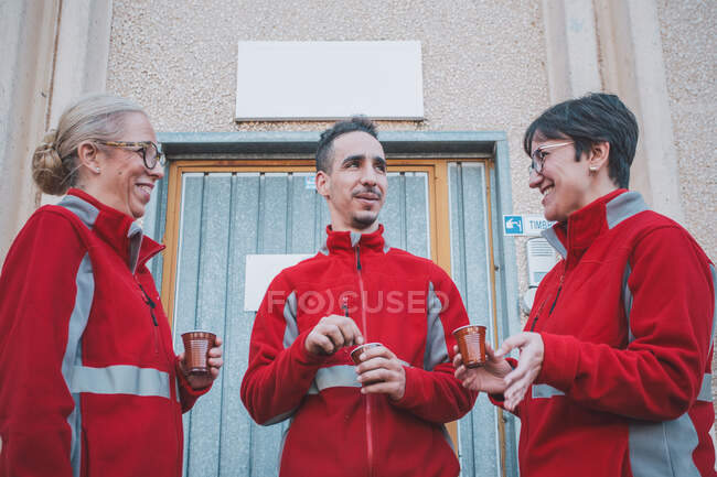Знизу чоловічі і жіночі колеги в червоній формі посміхаються і розмовляють з кавою в руках під час перерви — стокове фото