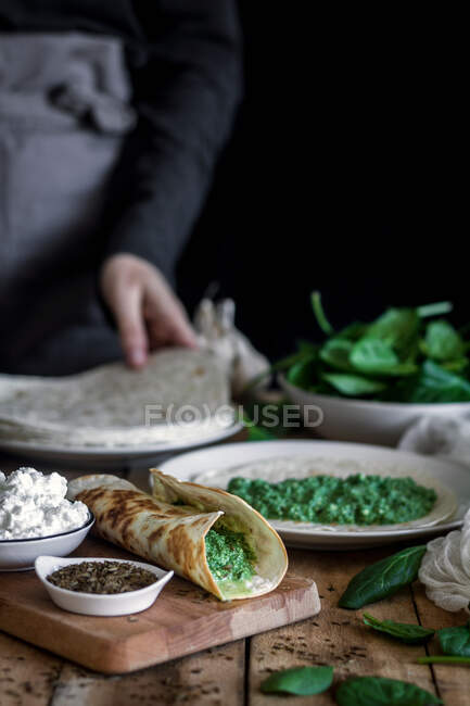 From above of tasty tortilla with puree of fresh spinach on wooden cutting board with faceless lady cooking on blurred background — Stock Photo