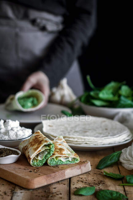 From above of tasty tortilla with puree of fresh spinach on wooden cutting board with faceless lady cooking on blurred background — Stock Photo