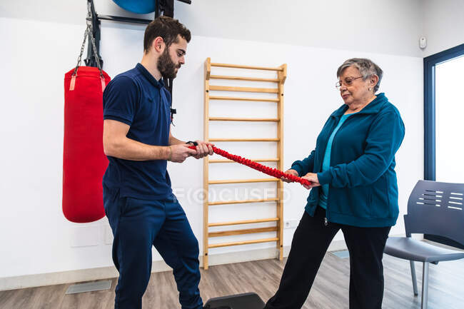 Entrenador de fitness y mujer mayor haciendo ejercicios de fisioterapia con plataforma escalonada y banda elástica - foto de stock