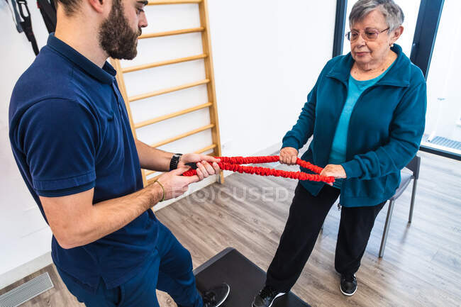 Fitness trainer and senior woman doing physiotherapy exercises with step platform and elastic band — Stock Photo