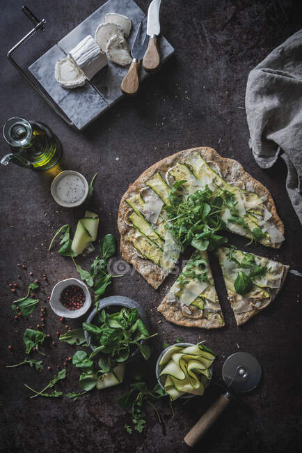 Зверху піца з зеленими скибочками кабачків на столі зі спеціями оливковий сир для вегетаріанської вечері — стокове фото