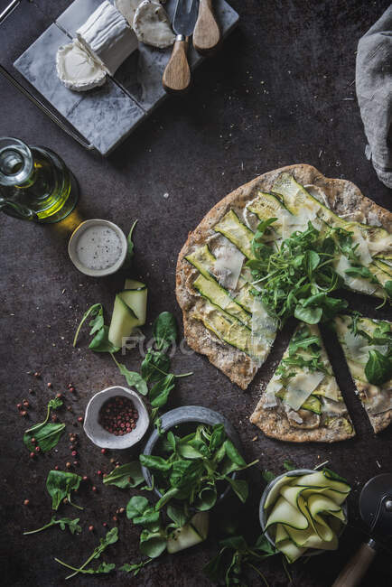 Зверху піца з зеленими скибочками кабачків на столі зі спеціями оливковий сир для вегетаріанської вечері — стокове фото
