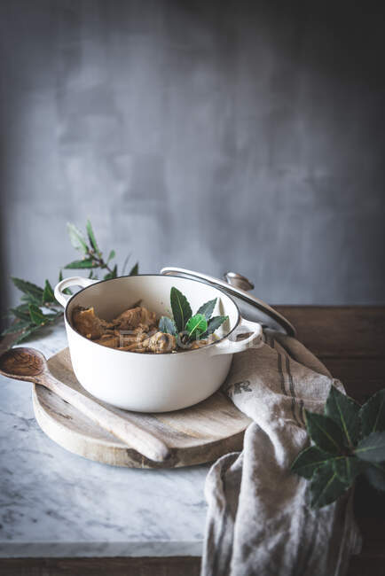 Dall'alto di pollo stufato con brodo in pentola decorata con foglie verdi su tavolo di marmo bianco — Foto stock