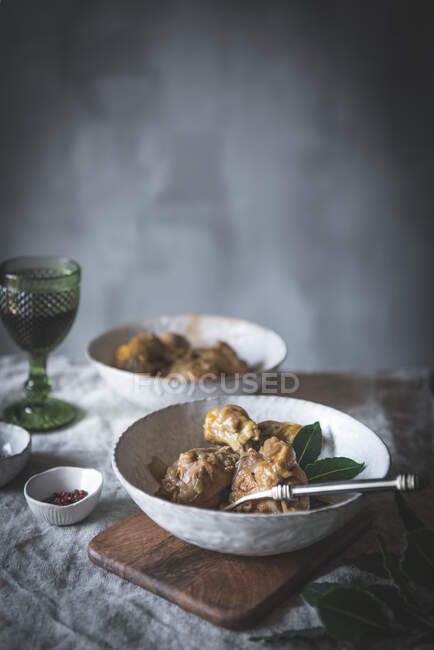 From above stewed chicken drumsticks with broth in white ceramic bowl decorated with greenery on table with spices and beverage — Stock Photo