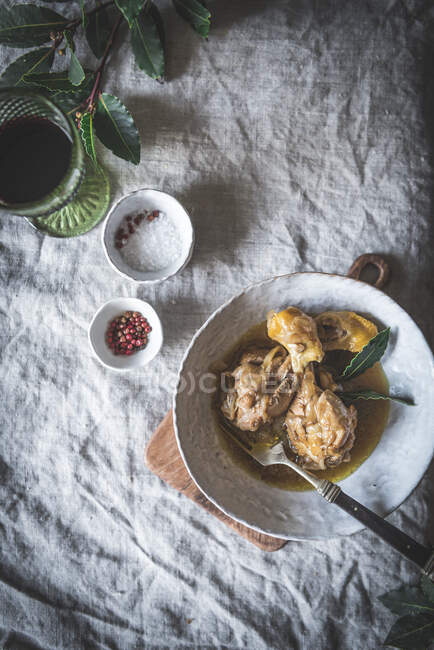 Top view of stewed chicken drumsticks with broth in white ceramic bowl decorated with greenery on table with spices and beverage — Stock Photo