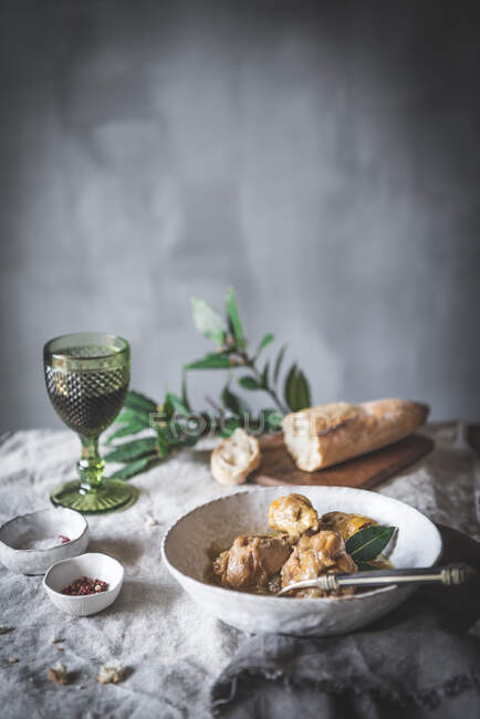 From above of stewed chicken drumsticks with broth in white ceramic bowl decorated with greenery on table with spices bread and beverage — Stock Photo