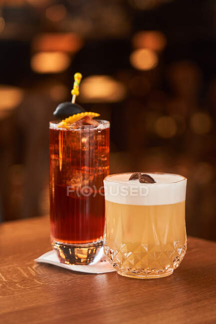 Cocktail com cubos de gelo decorados com pau com azeitona preta e Whiskey Sour com coquetel de suco de limão no balcão de madeira — Fotografia de Stock
