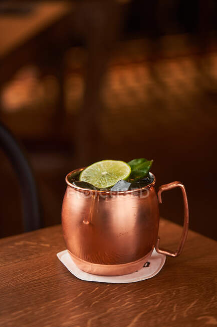 Classic alcohol cocktail Moscow Mule based on vodka with ginger beer and lime juice served in copper mug decorated with lemon slice on wooden table — Stock Photo