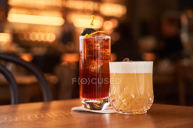 Cocktail with ice cubes decorated with stick with black olive and Whiskey Sour with lemon juice cocktail on wooden counter — Stock Photo