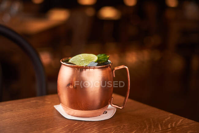 Classic alcohol cocktail Moscow Mule based on vodka with ginger beer and lime juice served in copper mug decorated with lemon slice on wooden table — Stock Photo