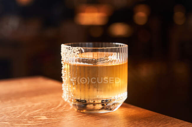Короткий келих бурштинового алкогольного коктейлю з льодом, прикрашений цукром, розміщений на дерев'яній стійці з чорним тлом — стокове фото