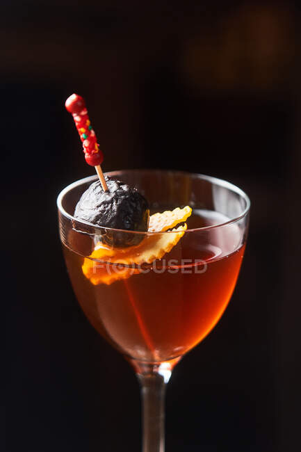Roter Alkohol-Cocktail Manhattan garniert mit Kirsche und orangefarbener Schale am Stock vor dunklem Hintergrund — Stockfoto