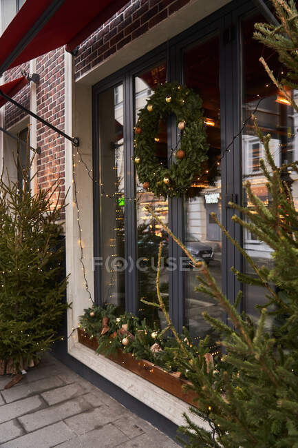 Facciata di caffè con decorazioni colorate di rami di conifere e albero di Natale con ghirlande alla luce del giorno — Foto stock