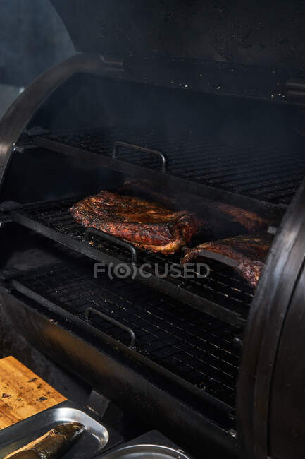 From above of smoking slices of meat on grill rack in barbecue — Stock Photo