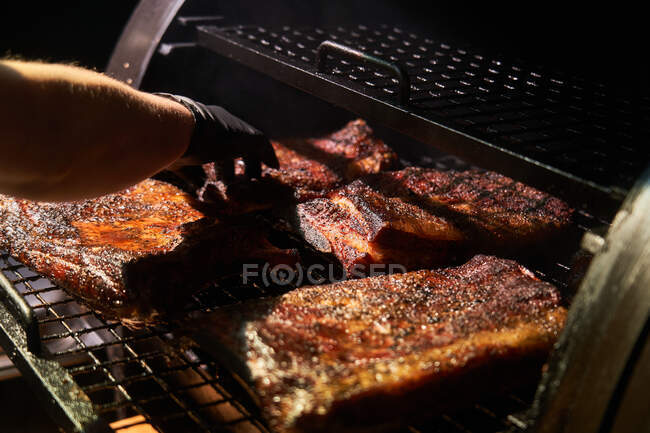 De arriba del cocinero de cosecha en guantes asar trozos de carne en el estante en la barbacoa - foto de stock