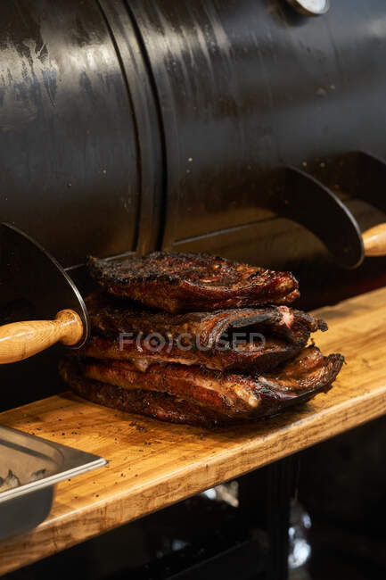 Composed stack of grilled juicy ribs on cutting board near barbecue — Stock Photo