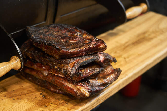 Composed stack of grilled juicy ribs on cutting board near barbecue — Stock Photo