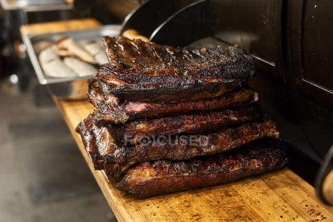 Pile composée de côtes juteuses grillées sur planche à découper près du barbecue — Photo de stock