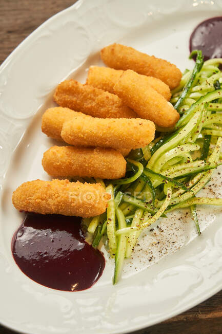 De haut bâtonnets de fromage frits avec du concombre tranché et sauce barbecue sur une assiette sur une table en bois — Photo de stock