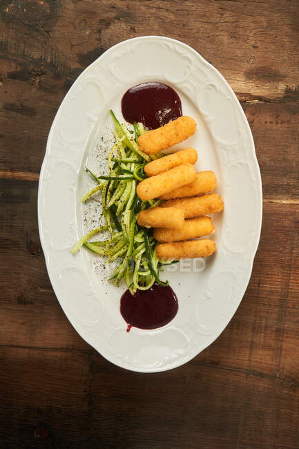 Top view of deep fried cheese sticks with sliced cucumber and barbecue sauce on plate on wooden table — Stock Photo