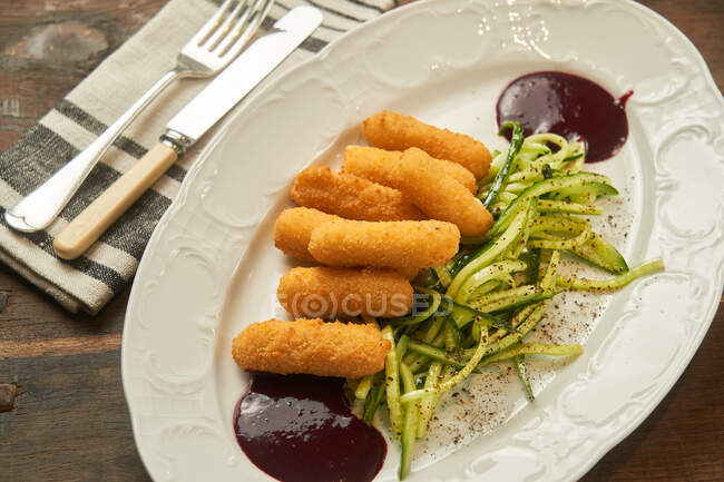 From above deep fried cheese sticks with sliced cucumber and barbecue sauce on plate on wooden table — Stock Photo
