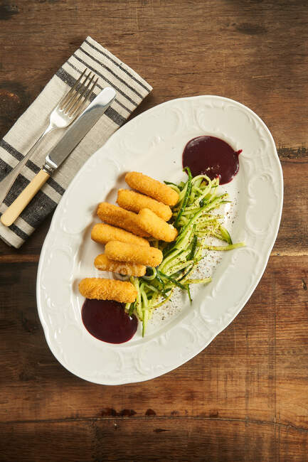 Vue du dessus des bâtonnets de fromage frits avec du concombre tranché et de la sauce barbecue sur une table en bois — Photo de stock