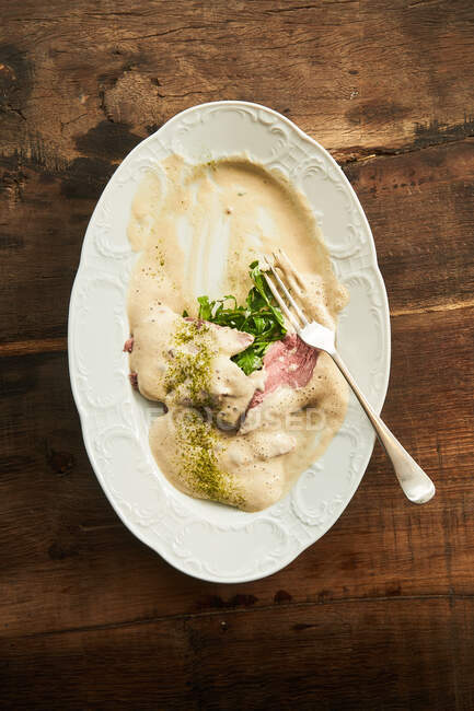 Верхний вид на остатки вкусной еды из красной рыбы с белым соусом и зеленью на тарелке на деревянном столе — стоковое фото