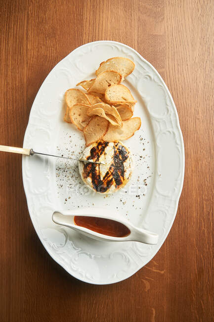 De arriba deliciosa hamburguesa de pollo a la parrilla con chips de pan crujiente horneado y salsa barbacoa en el plato en la mesa - foto de stock