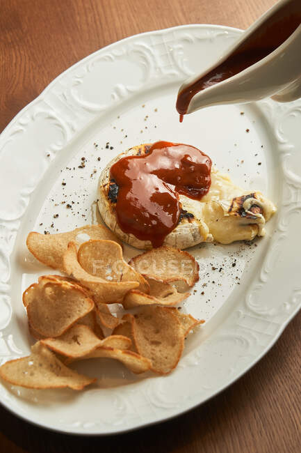 From above unrecognizable person pouring BBQ sauce on delicious grilled cream cheese and baked bread chips on plate on table — Stock Photo