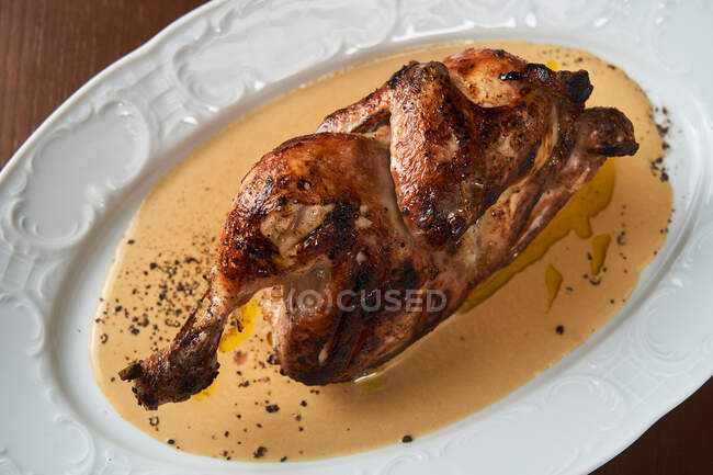 From above cooked tasty grilled whole chicken serving on white plate on table — Stock Photo