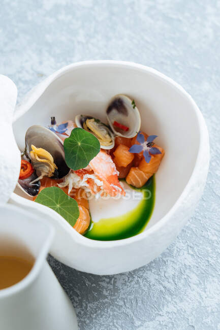 De arriba la sopa sabrosa de los mariscos con el salmón y las almejas adornadas con las flores en la escudilla a la mesa - foto de stock