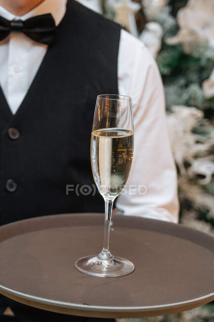 Serveur masculin méconnaissable tenant un plateau avec un verre de vin blanc pendant la fête au restaurant — Photo de stock