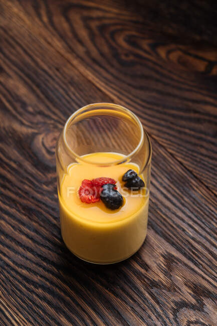 From above natural healthy milk cocktail decorated with berries on top in glass jug on wooden table — Stock Photo