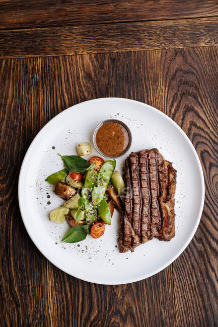 Vue du dessus du steak de bœuf grillé au basilic et légumes servi dans une assiette avec sauce barbecue — Photo de stock