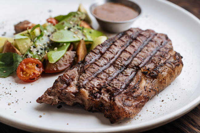 De haut gros plan de steak de bœuf grillé avec du basilic et des légumes servis dans une assiette avec sauce barbecue — Photo de stock