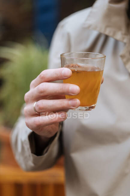 Homme sans visage tenant boisson alcoolisée dans une tasse en verre pendant la fête dans un café — Photo de stock