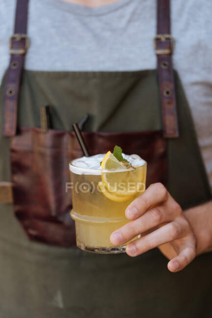 Куст бариста в фартуке держа стакан свежего сочного лимонада украшенный лимоном и зеленой мятой — стоковое фото