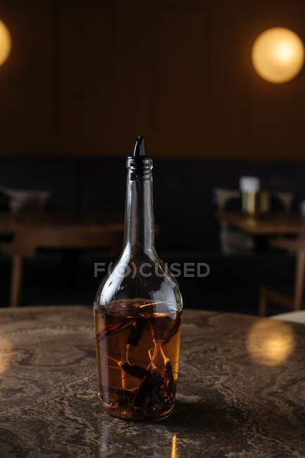 Aged alcohol with dried black pepper in shiny glass bottle at dark bar in warm light — Stock Photo