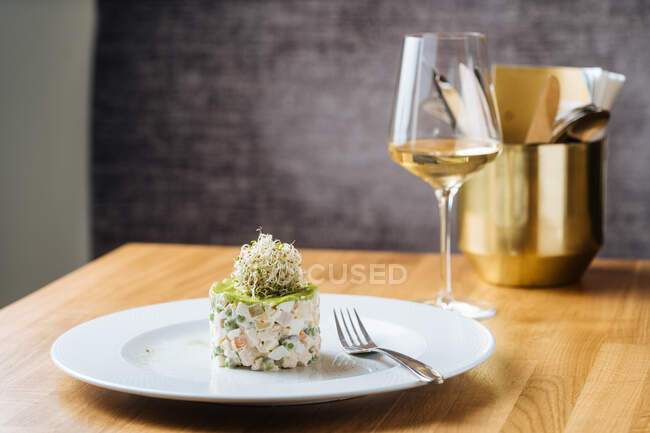 Tasty fresh vegetable salad with decoration on top in white plate on wooden table served with glass of wine in restaurant — Stock Photo