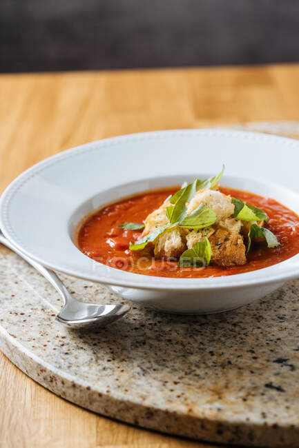 Червоний апетитний свіжий томатний суп з зеленню на білій тарілці на мармуровій підставці в кафе — стокове фото