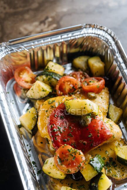 Von oben reife Scheiben rote Tomaten Zucchini mit Kräutern und Soßen in glänzender Backform auf den Tisch streuen — Stockfoto