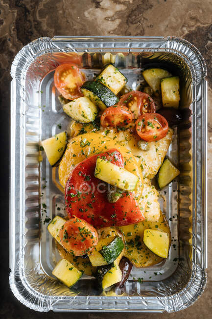 From above ripe slice red tomatoes zucchini sprinkled with herbs and sauces in shiny baking form on table — Stock Photo