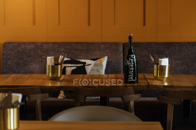 Dark bottle on yellow able surrounded by chairs in elegant interior of stylish restaurant with warm light of fashion round lamp — Stock Photo