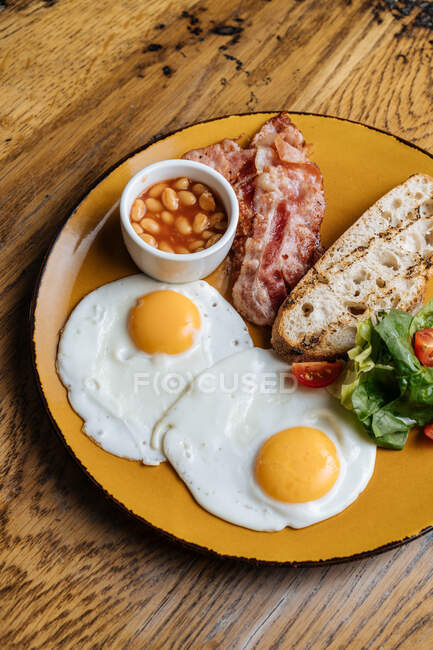 De acima mencionado apetecendo ovos fritos bacon milho em verdes de tomate na chapa amarela com bebida no café — Fotografia de Stock