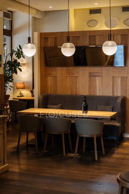Dark bottle on yellow able surrounded by chairs in elegant interior of stylish restaurant with warm light of fashion round lamp — Stock Photo
